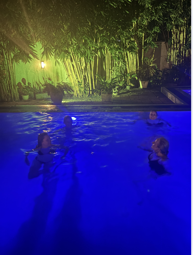 Guests swimming in the illuminated villa pool at night beside the bamboo garden