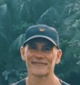 James smiling in a cap against tropical greenery